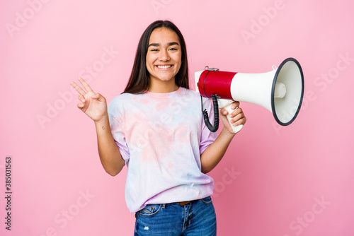 Young asian woman holding a megaphone isolated on pink background joyful and carefree showing a peace symbol with fingers.