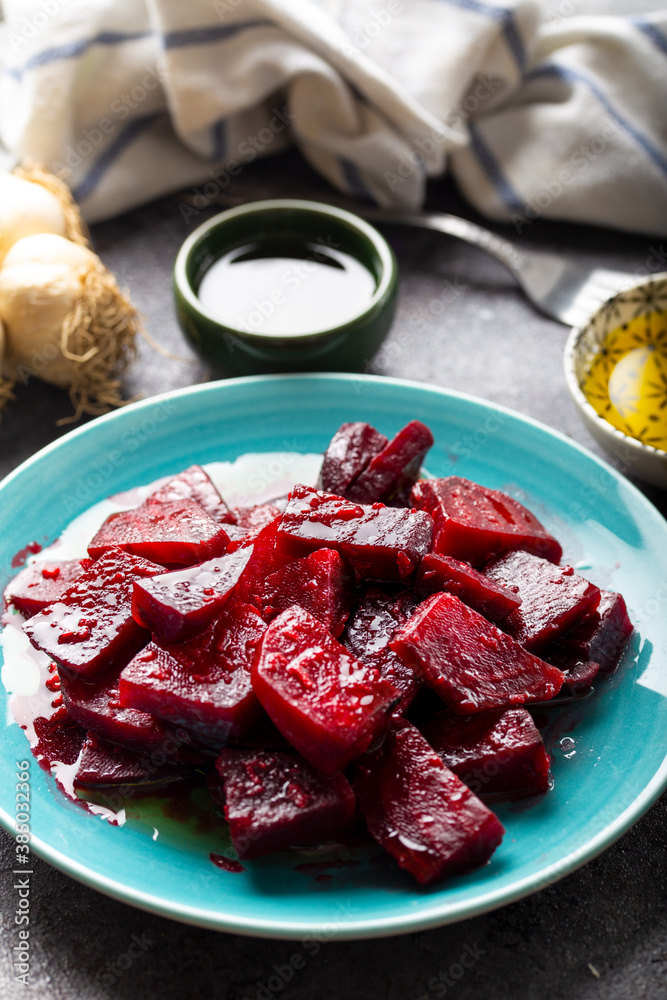 Beetroot salad with garlic and olive oil sauce in dish on dark background.