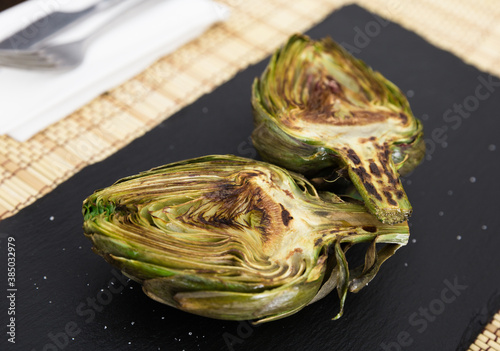 cooked fried halves artichokes on black stone board