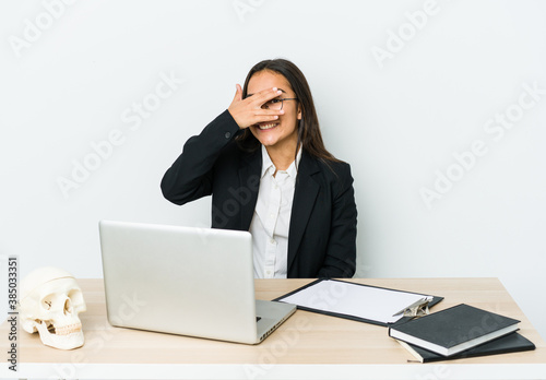 Young traumatologist asian woman isolated on white background blink at the camera through fingers, embarrassed covering face.