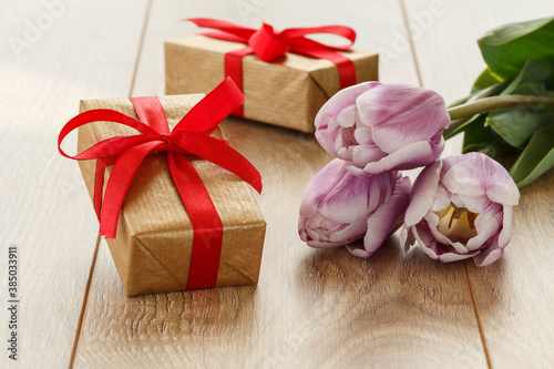 Gift boxes with red ribbons and tulip flowers on wooden boards.