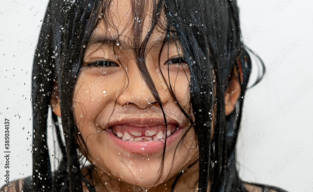 Close up cute face of Asian child girl, happy face under shower rain on white background, big smile on face, wet and water drop on skin.