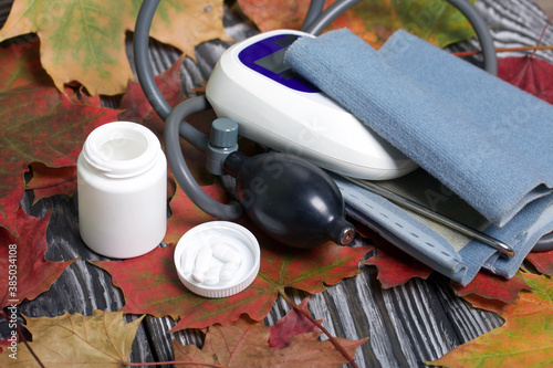 Tonometer for measuring blood pressure. Nearby is a container with pills. Among the autumn maple leaves.