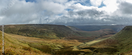 A scenic panorama view of a mountain valley with green slopes under a stormy grey sky and some white clouds