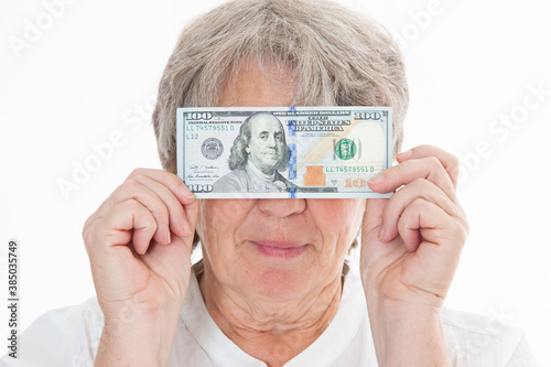 Seniorin hält sich Geld vor ihr Gesicht vor weißem Hintergrund