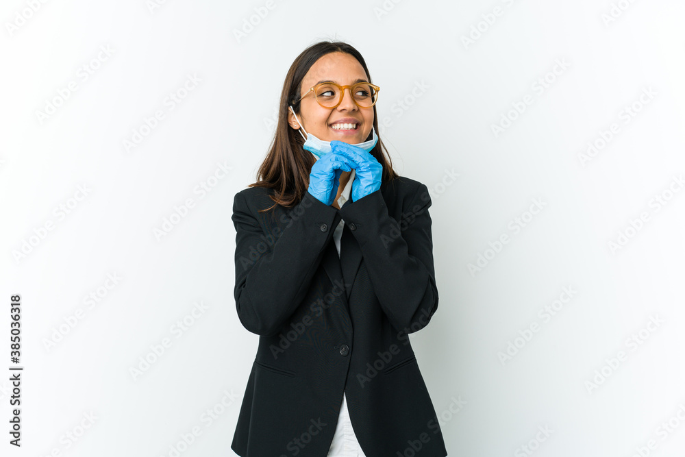 Young business latin woman wearing a mask to protect from covid isolated on white background keeps hands under chin, is looking happily aside. Young business latin woman wearing a mask to protect from covid isolated on white background keeps hands under chin, is looking happily aside.