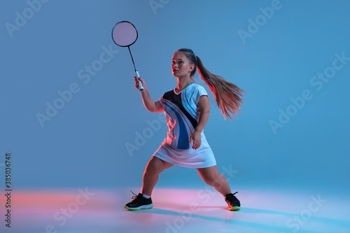 High up. Beautiful dwarf woman practicing in badminton isolated on blue background in neon light. Lifestyle of inclusive people, diversity and equility. Sport, activity and movement. Copyspace. photo