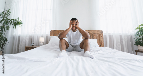 Stressed Overslept African American Man Sitting In Bed At Home