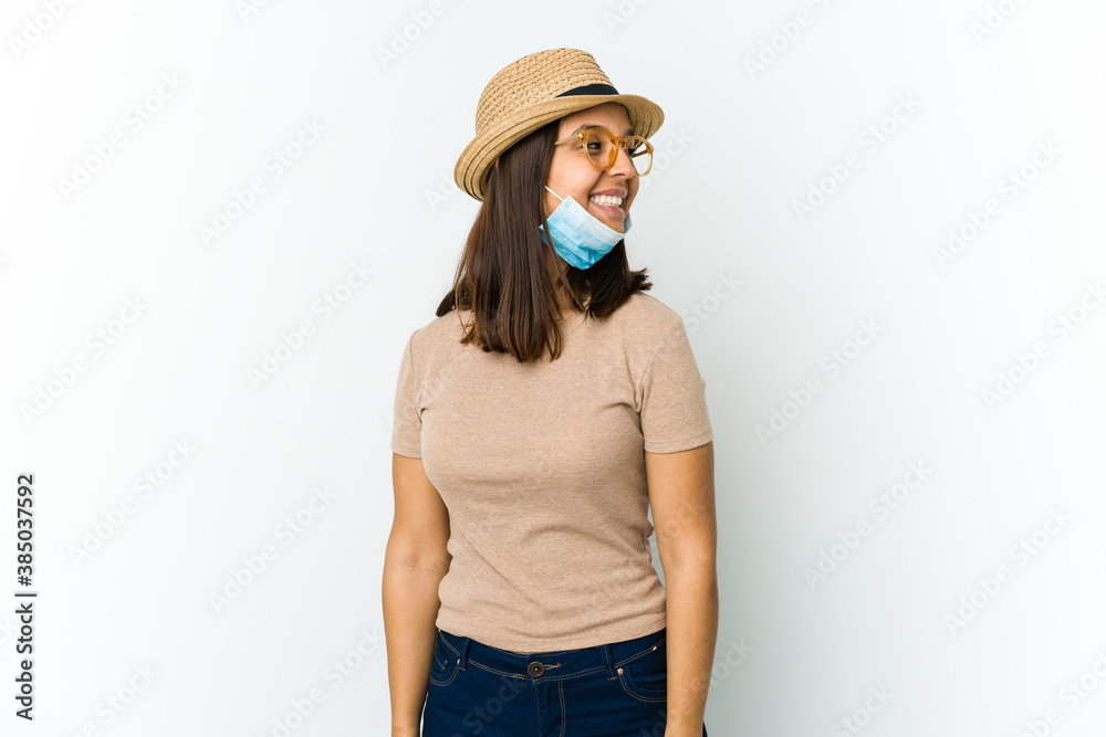 Young latin woman wearing hat and mask to protect from covid isolated on white background looks aside smiling, cheerful and pleasant. Young latin woman wearing hat and mask to protect from covid isolated on white background looks aside smiling, cheerful and pleasant.