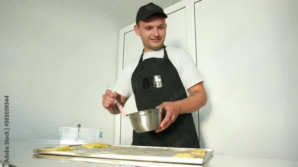 Lubricate with a brush the prepared mixture of raw dough for making buns, cookies. Baker male man makes fresh scone paste at table in bakery kitchen. Lubricate with a brush the prepared mixture of raw dough for making buns, cookies. Baker male man makes fresh scone paste at table in bakery kitchen.