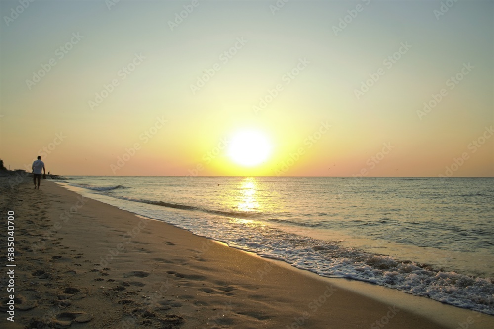 
A man walking along the beach at sunset