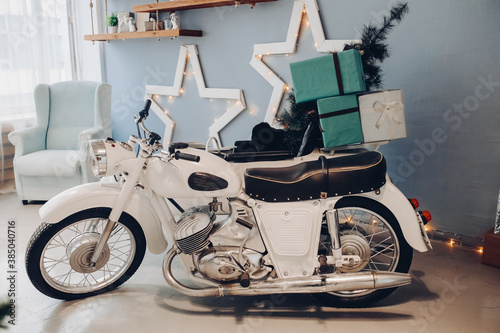 Stock photo of white motorcycle with minuature Christmas tree and wrapped Christmas presents in cradle. Atmospheric interior for Christmas Day. 2020 New Year. photo