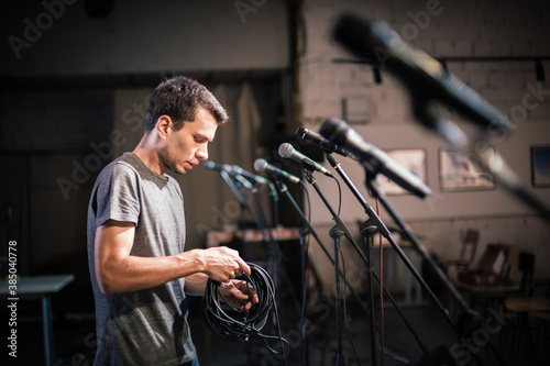 Theater audio technician adjusting an microphones on the scene. Installing and testing the sound system in the background