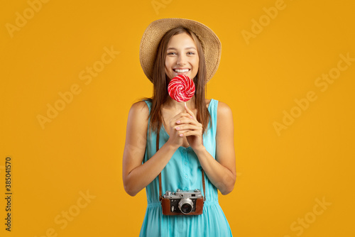Pretty lady traveller eating candy, yellow background