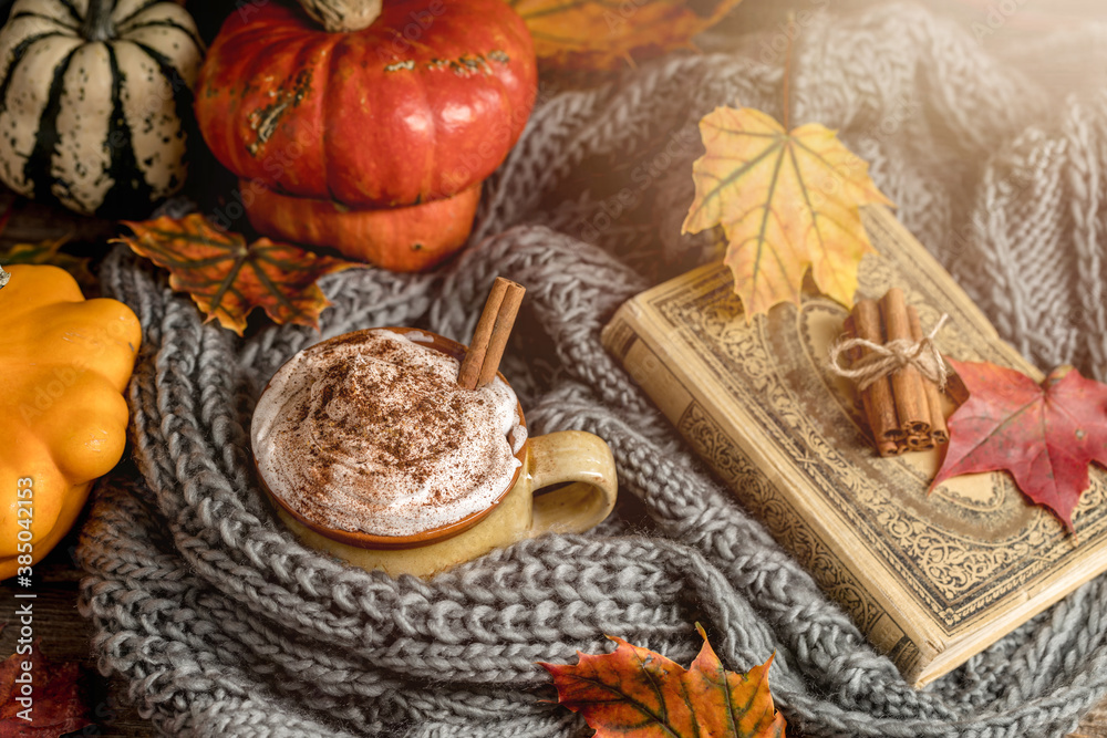 Autumn concept, still life of pumpkin spice latte with whipped milk cream and cinamon. Colorful pumpkins and dry leaves. Old natural wood backround