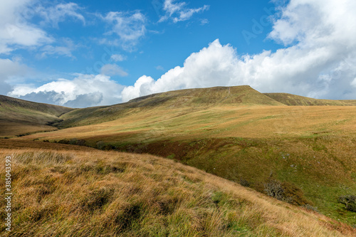 A scenic view of a mountain valley with green slopes under a beautiful blue sky and some white clouds