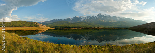 Panorama of a mountain lake against the background of snow-capped peaks. Reflection in water. Altai, Russia.