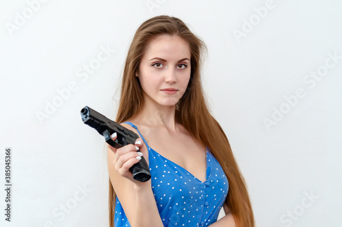 Sexy European woman with long hair and fair skin is holding a gun and looks straight into the camera.