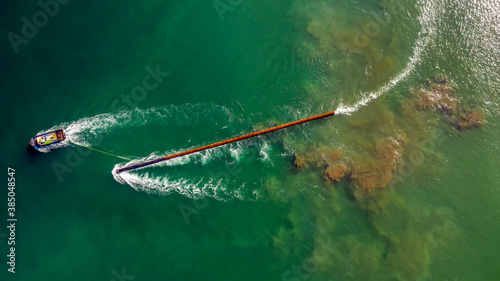 Aerial view of the boat during carry a long pile (stake) on the water to build pier.