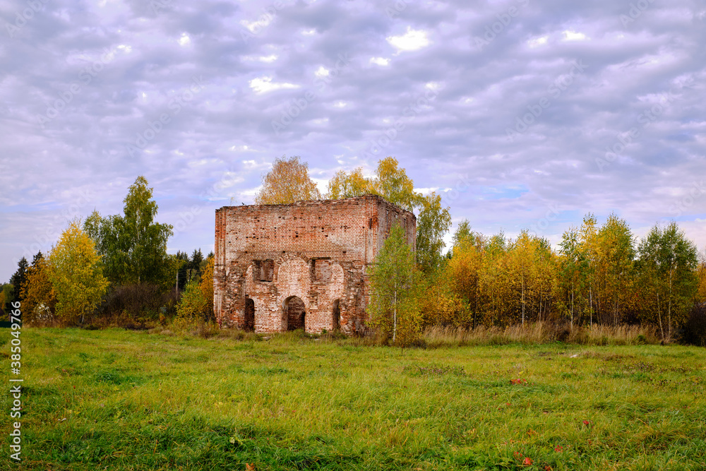 The ruins of an old red brick building surrounded by trees, autumn day.
