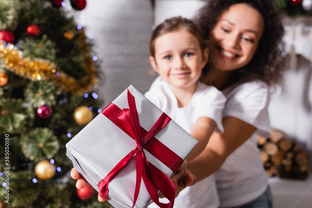 Selective focus mother hugging daughter with gift box near festive pine at home Selective focus mother hugging daughter with gift box near festive pine at home