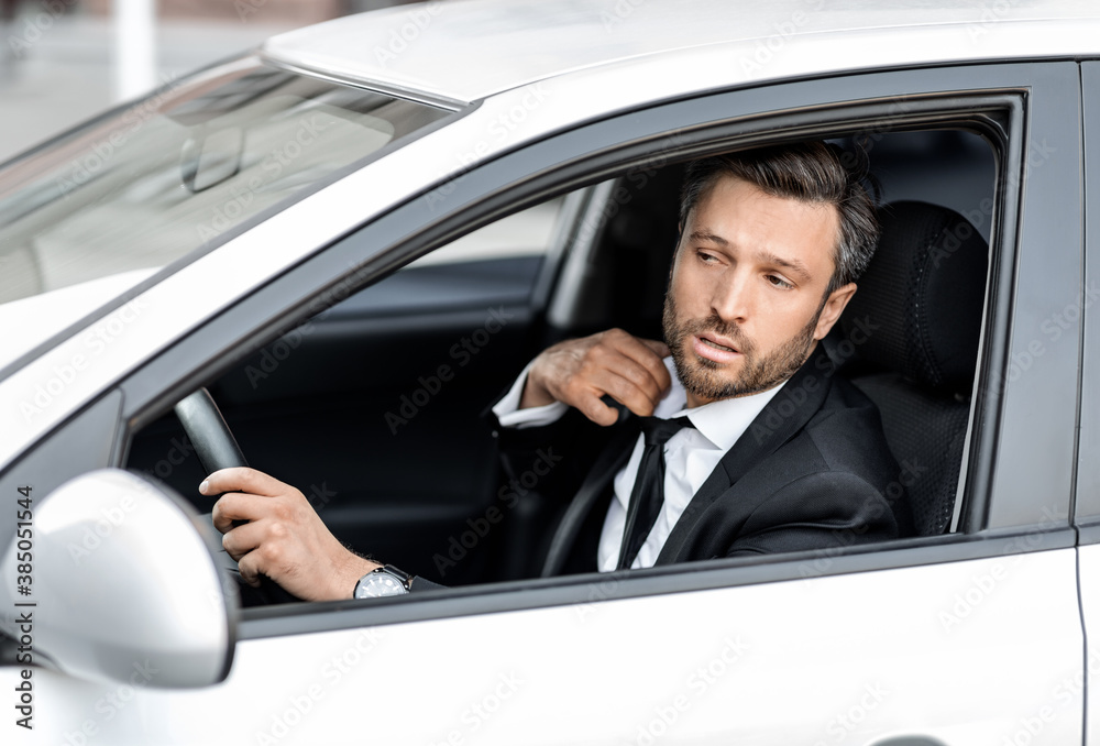 Stressed businessman driving car, lowering his tie