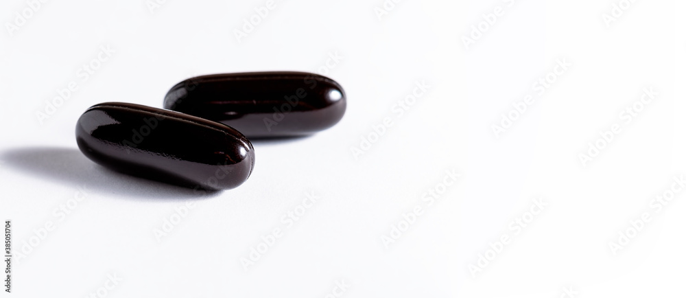 Big black soft gel medical capsules on white background. Long banner format. Health care and immunity support concept. Big black soft gel medical capsules on white background. Long banner format. Health care and immunity support concept.
