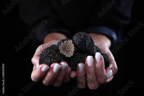 A handful of black truffles in a woman's hands. Exquisite and fragrant mushroom. Unrecognizable person. Black background. Close up. Copy space. photo