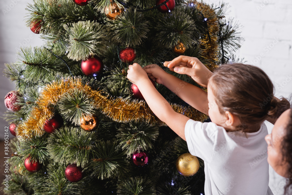 Mother and daughter decorating pine with christmas balls at home