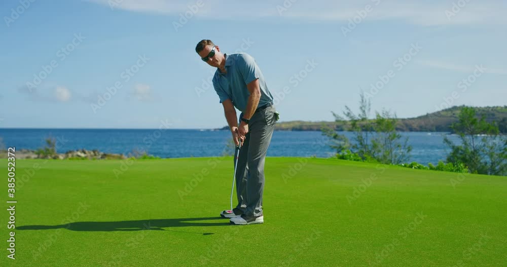 Man playing golf on beautiful course by the ocean, putting on the green into the hole Man playing golf on beautiful course by the ocean, putting on the green into the hole