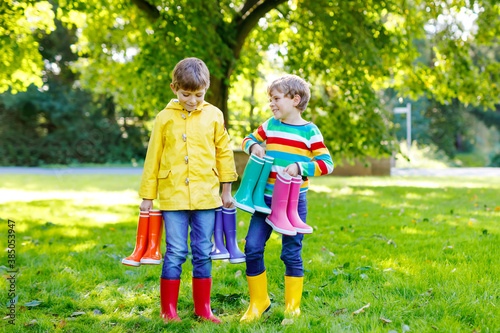 Two little kids boys, cute siblings with lots of colorful rain boots. Children in different rubber boots and jackets. Footwear for rainy fall. Healthy twins and best friends having fun outdoors