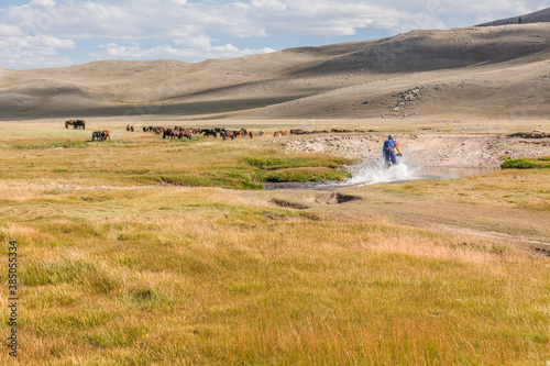 a motorcyclist tries to drive along a road filled with water during a flood after rain. Horses on the back plane