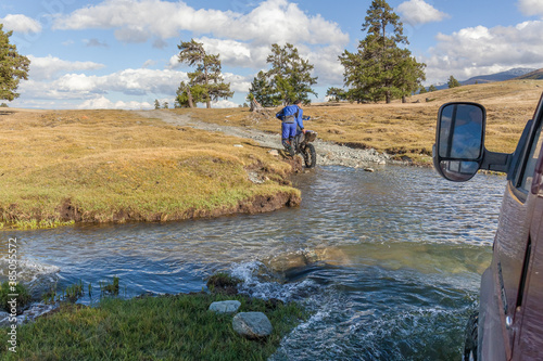 A motorcyclist pushes a motorcycle along a road flooded with water. Altai, Mongolia.