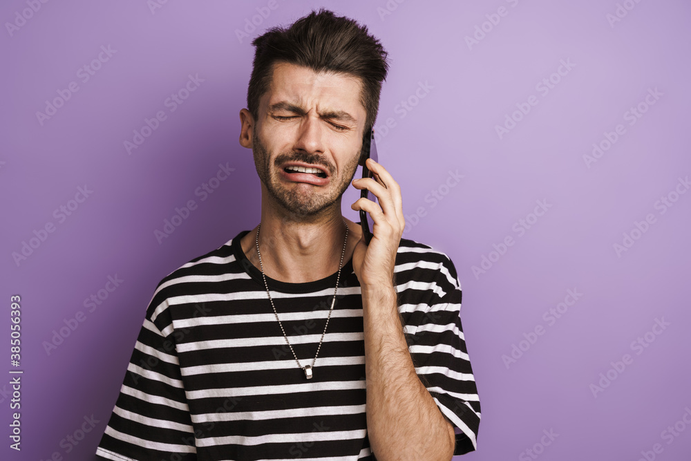 Photo of unhappy brunette man crying while talking on mobile phone