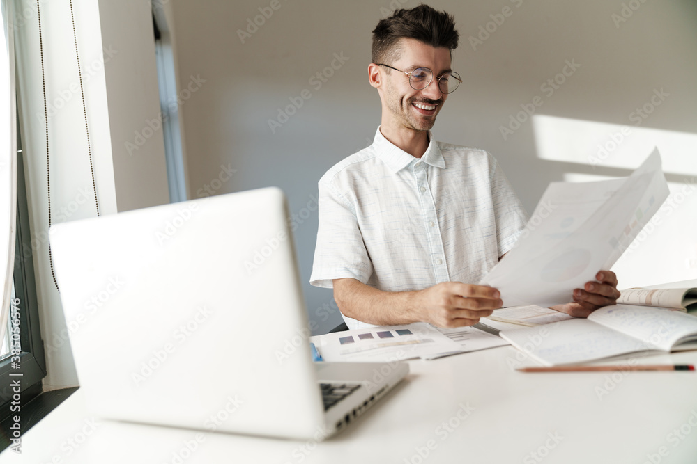 Photo of smiling unshaven man working with laptop and papers at table Photo of smiling unshaven man working with laptop and papers at table