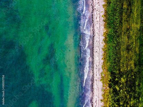 Top down aerial view of a sandy beach in the summer with waves crashing ashore.