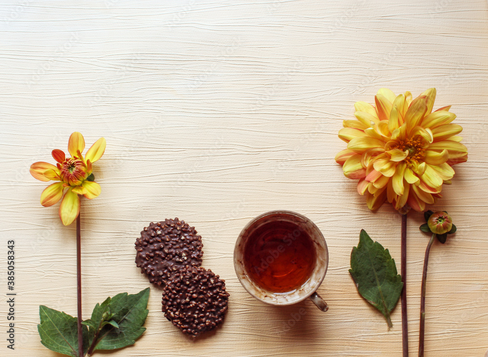 A Cup of tea with chocolate cookies and two yellow Dahlia flowers on a light background, close - up, top view , space for text-the concept of a good start to an autumn day A Cup of tea with chocolate cookies and two yellow Dahlia flowers on a light background, close - up, top view , space for text-the concept of a good start to an autumn day