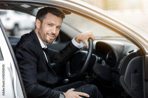 Happy young entrepreneur sitting in car, driving to airport