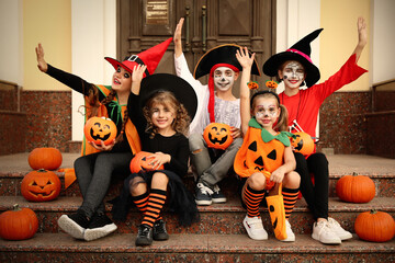 Cute little kids with pumpkins wearing Halloween costumes on stairs outdoors