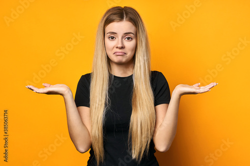 surprised blonde on a yellow background, throws up her hands to the side