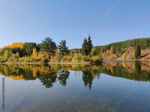 reflection in the water of trees by the lake in the autumn landscape