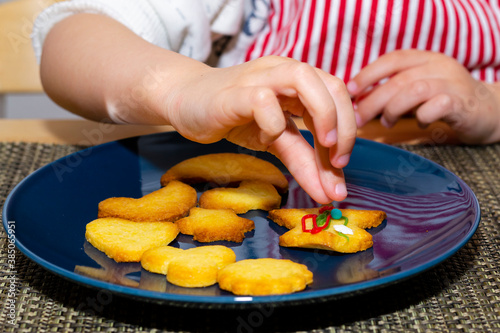 Close up view of kid’s hands decorating homemade cookies for holidays. A child decorates cookies with edible colorful sugar pearls.