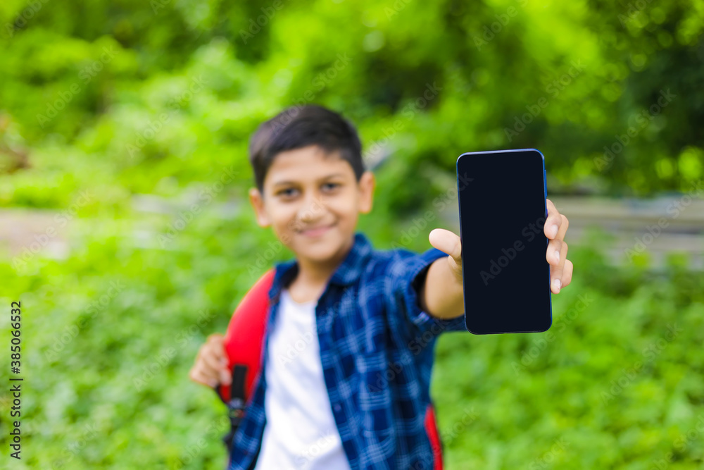 technology concept: Cute indian little school boy holding bag and showing smartphone