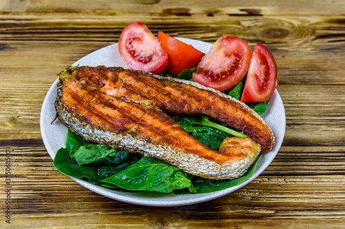 Plate with roasted salmon steak, tomtoes and spinach leaves on a wooden table photo