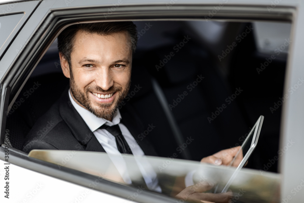 Smiling rich businessman in suit sitting in car