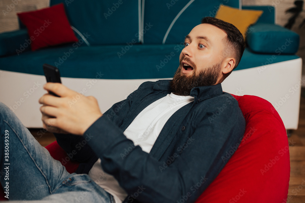Fototapeta premium Young man in modern interior design looking agitated at display of her smartphone, impressed by media content from web.
