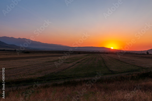Sunset in the mountains. Autumn field in the foreground and mountains against the backdrop of the red sky and the setting sun. Kyrgyzstan.