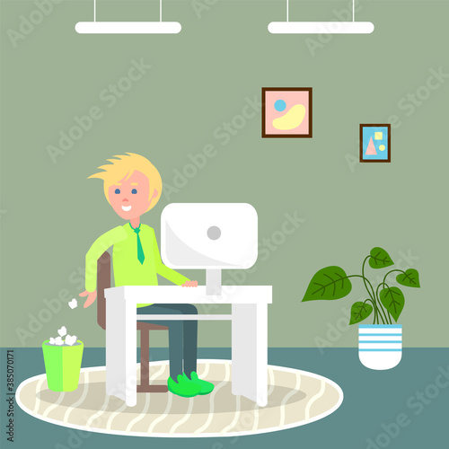 Young blond guy sitting at white stylish table with white monoblock. The guy throws crumpled paper lumps into trash. Round rug, green walls and floor, potted plant, ceiling lighting. Work at home