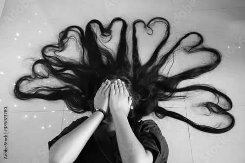 Black and white photo of a woman hiding face with failed attempt to make heart shapes with her long hair on the ground  photo