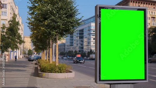 Green screen billboard located on a busy street. Cars are moving in a traffic jam. Morning of a working sunny day.